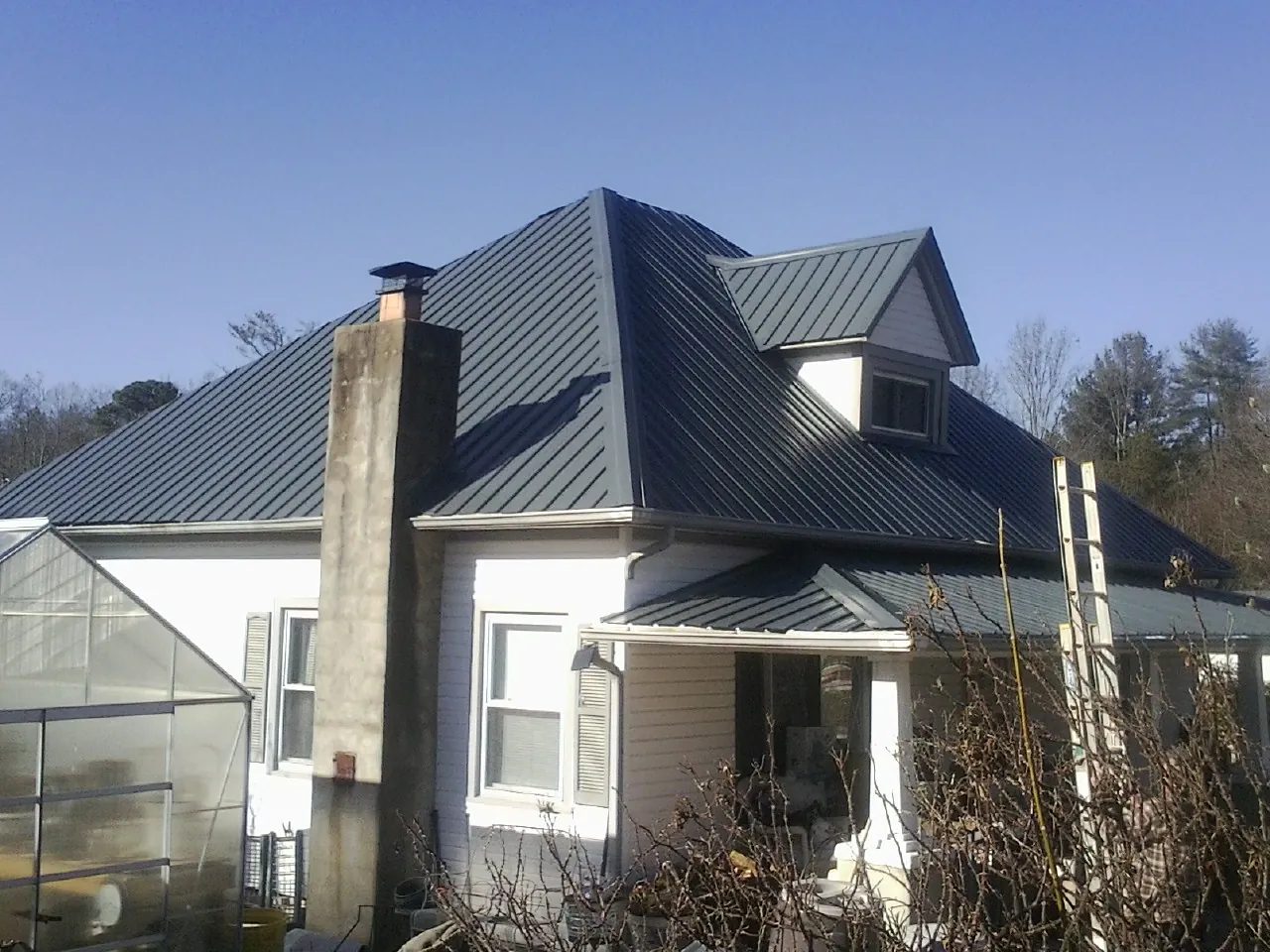 Dark blue standing seam metal roof on a white farmhouse with dormer — Slate & Tile Roof Repair by Roofing Brothers in Carsonville