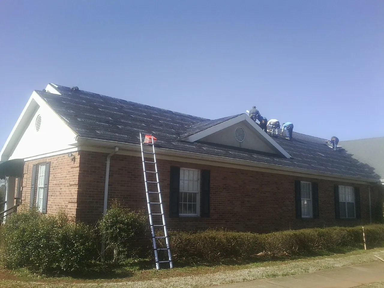 Crew tearing shingles off a brick ranch roof with a ladder set — Emergency Roof Repair work by our crew in Carsonville