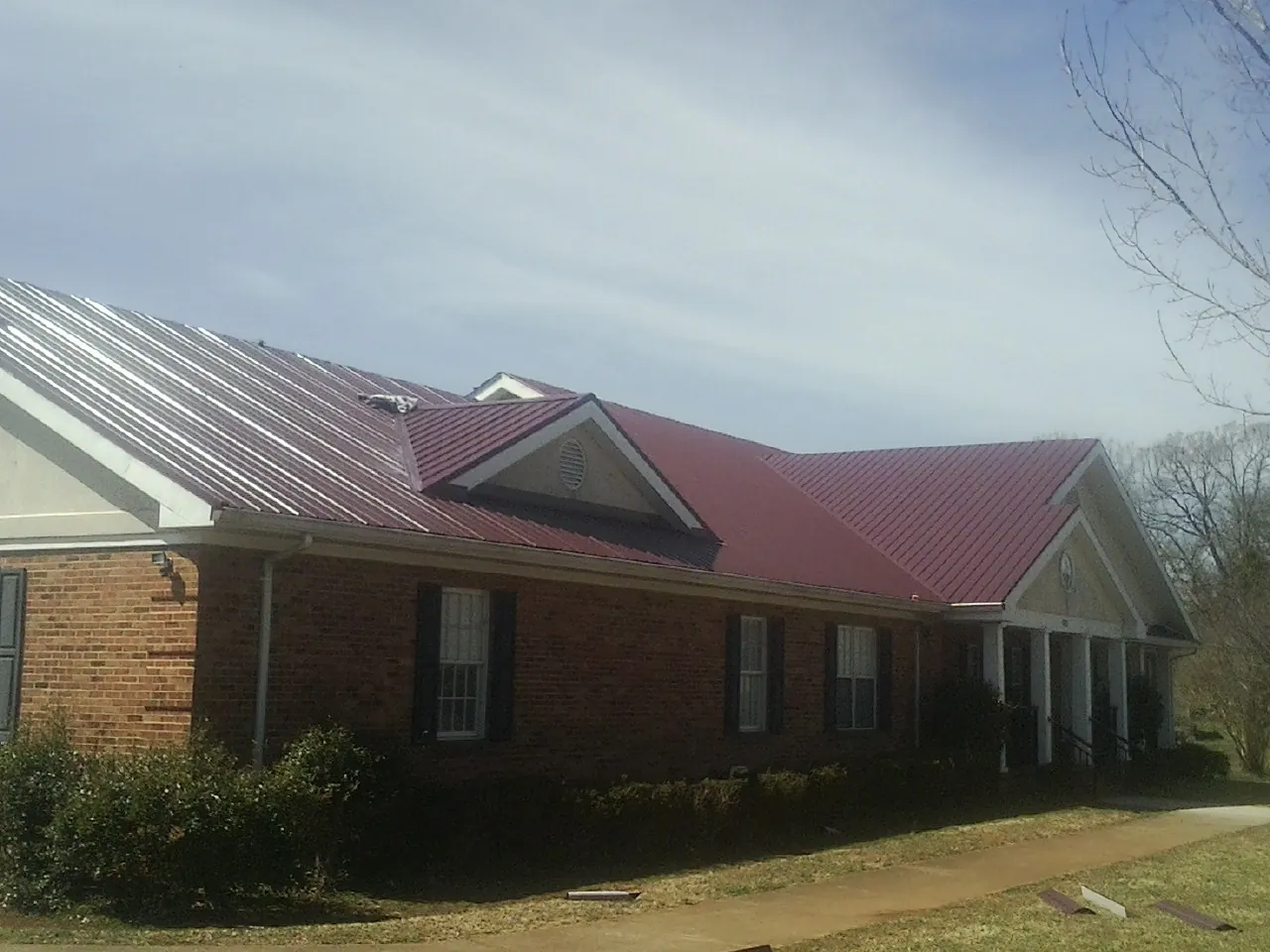 Red metal roof with gabled entries on a long brick building, from a Hail Damage Roof Repair job in Carsonville