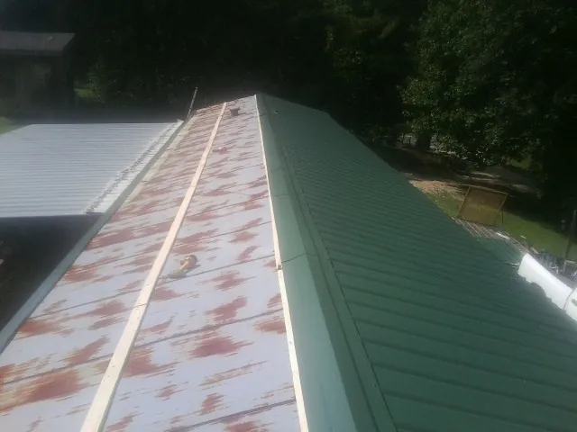 Old rusted panels beside newly installed green metal roofing — Wind Damage Roof Repair by Roofing Brothers in Carsonville
