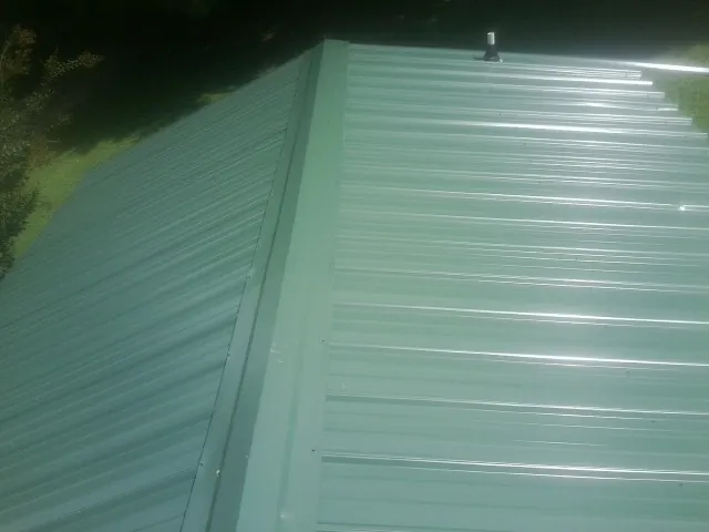 New green metal panels meeting at the ridge of a roof — Flat Roof Repair work by our crew in Carsonville