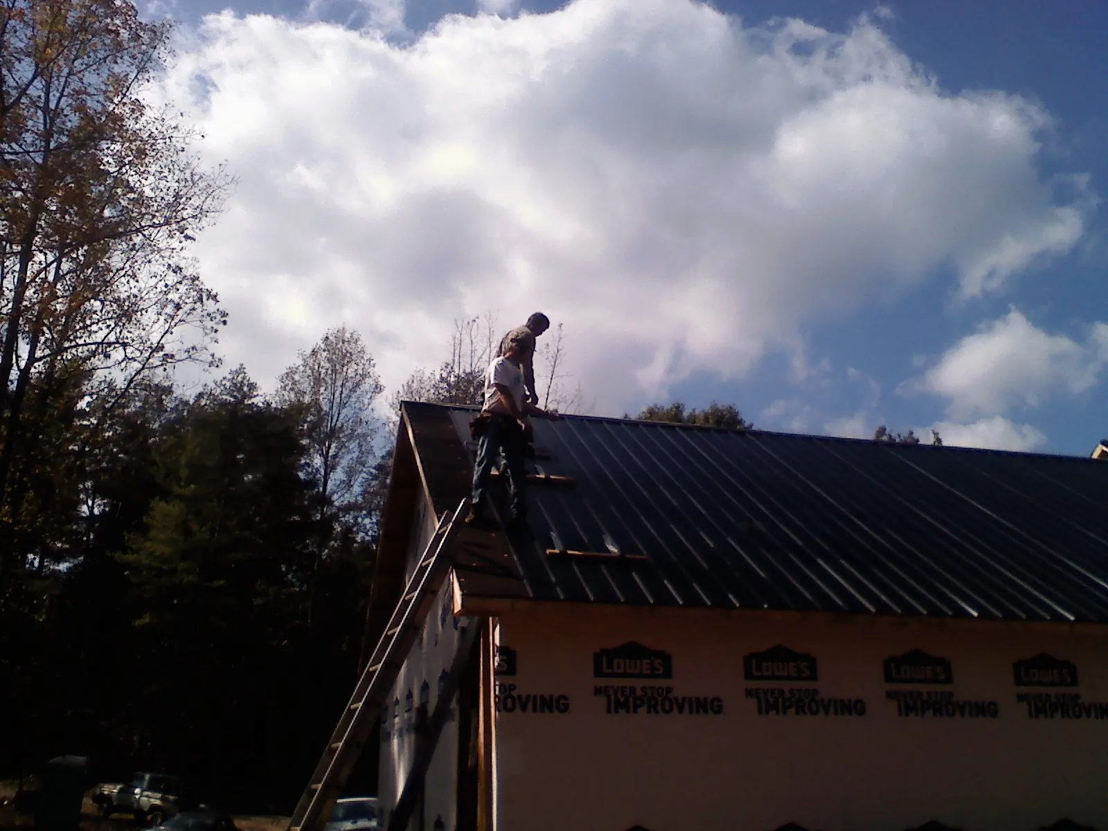 Roofer fastening dark metal panels high against a cloudy sky, from a Roof Inspection job in Carsonville