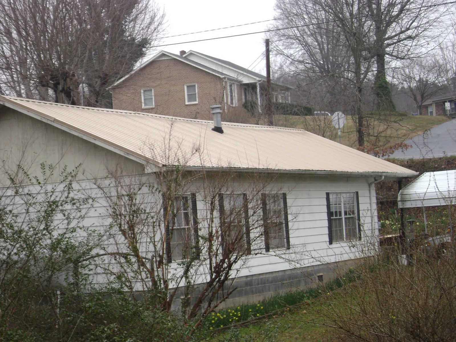 Tan metal roof on a white sided house set into a hillside — Commercial Roofing by Roofing Brothers in Carsonville